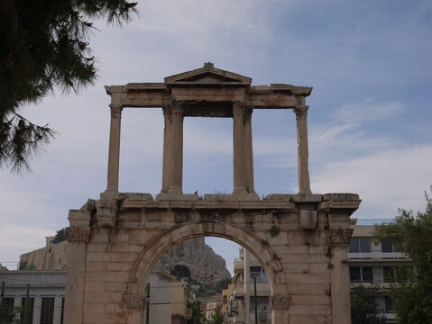 View of Hadrian's Arch with the ancient Acropolis visible in the background under a clear blue sky in Athens, Greece.