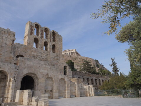 View of the ancient stone arches of the Odeon of Herodes Atticus with the Parthenon visible on the Acropolis hill in Athens, Greece.