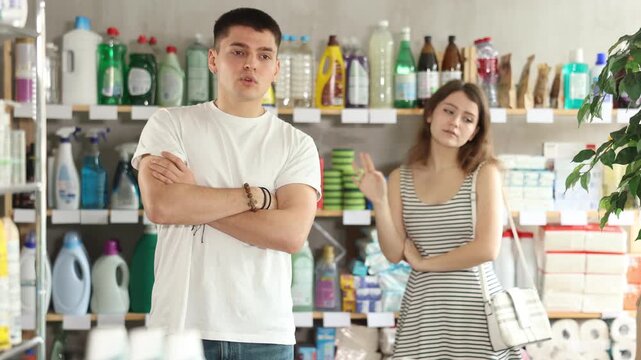 Spouses yell at each other in sales area of household store. Angry and stubborn guy and girl are indignant and swear, family conflict. Couple is arguing and yell at each other