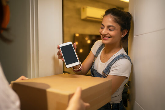 Young woman accepting delivery package at the doorstep with mobile in hands.
