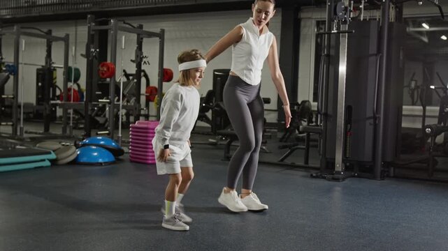 Caucasian young adult female trainer instructing Caucasian child boy during lunges workout in gym. Video suitable for family fitness marketing, youth sports coaching, and wellness campaigns