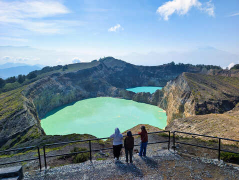 View of Kelimutu National Park with its vibrant turquoise crater lakes and visitors standing at the viewing platform in Detusoko, East Nusa Tenggara, Indonesia.