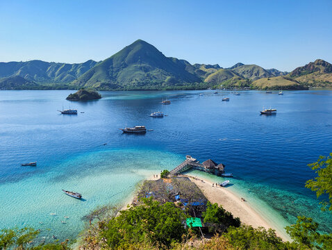 View of Pulau Kelor with its turquoise waters, wooden jetty, and traditional boats surrounded by lush green hills in Komodo, East Nusa Tenggara, Indonesia.