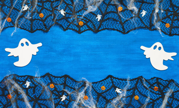 Halloween background - blue wooden rustic surface with white ghosts decorations, black lace spiderweb, festive Halloween border with free space for text