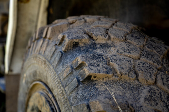 Close-up of a dirty off-road truck tire tread covered with dried mud and soil, showing texture, heavy vehicle wheel, and automotive mechanics.