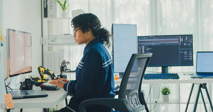 Young African American female robotics engineer coding AI software for robotic arm in laboratory. Embedded system, firmware testing, machine learning, industrial automation, future technology concept.
