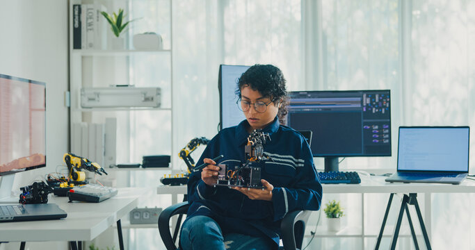 Young African American female robotics engineer discussing mechanical part on video call and looking at camera in laboratory. Remote work, virtual training, online meeting, future technology concept.