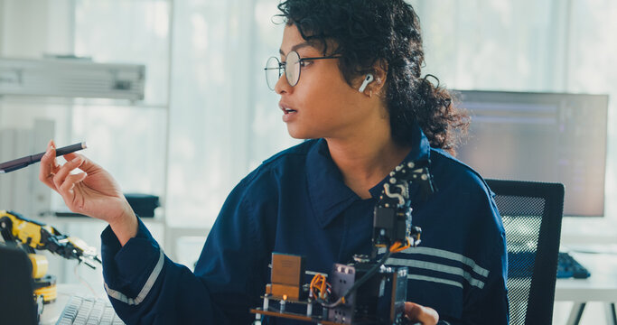 Young African American female robotics engineer discussing mechanical part on video call in laboratory. Remote work, virtual training, online meeting, future technology, technical support concept.