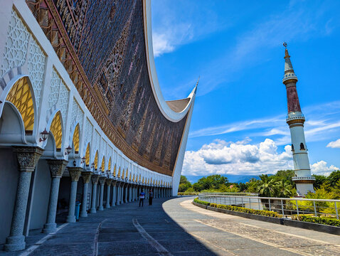 View of the Great Mosque of West Sumatra with its iconic curved roof and tall minaret under a bright blue sky in Padang, West Sumatra, Indonesia.