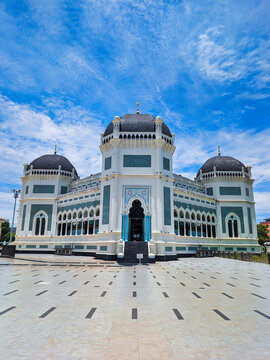 View of the Great Mosque of Medan with its ornate domes and white and green facade under a bright blue sky in Medan, North Sumatra, Indonesia.