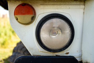 Close-up of a vintage round glass headlight and orange turn signal lamp mounted on the white metal fender of a heavy truck outdoors. © Marina