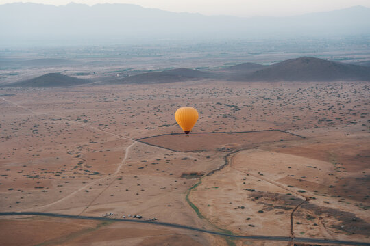 View of a yellow hot air balloon floating over the arid desert landscape with the Atlas Mountains in the distance, Marrakesh, Marrakesh-Safi, Morocco.
