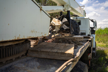 Fototapeta premium Truck crane flatbed platform with hoist mechanism, steel chains, wooden supports, and boom structure outdoors in daylight, showing heavy construction transport and rigging equipment.