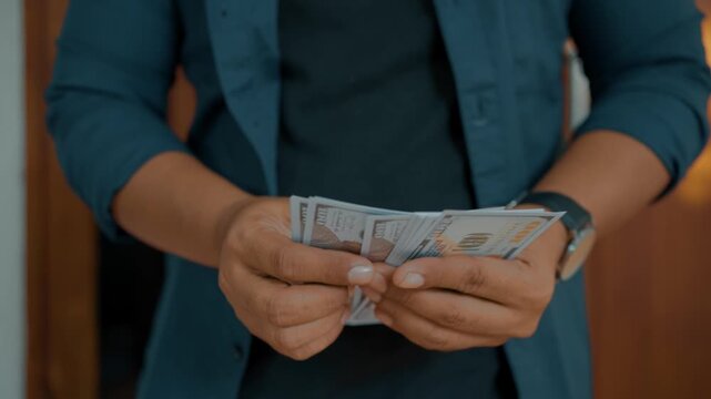 Man investor counting US Dollar bills, close-up. Male trader holds bundle of money, Considers USD at home. Person manages budget.