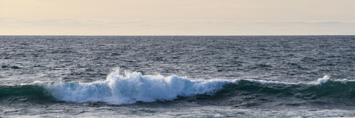 Fototapeta premium Panoramic ocean scene showing a powerful wave breaking across textured open water beneath a clear horizon. Extra-wide composition with copy space designed for website banners, headers, advertising, pr