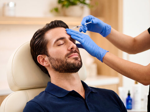 Man receiving cosmetic injection in forehead from practitioner wearing blue gloves
