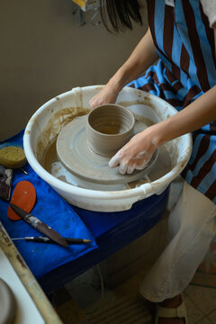 Close up of a professional female potter using a wire thread to cut a freshly thrown clay pot from a spinning pottery