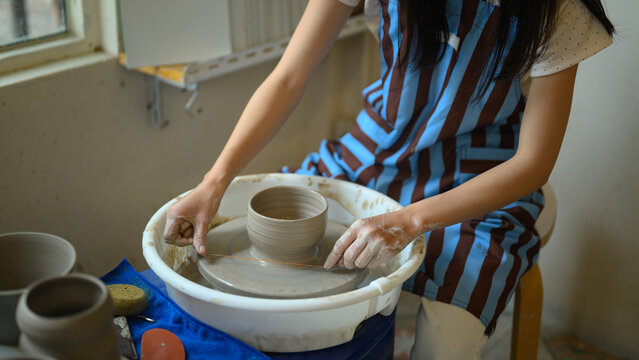 Female Potter Cutting Clay Pot from Pottery Wheel with Wire Thread in Ceramic Workshop