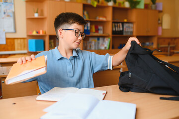 Young boy packing book into backpack in classroom