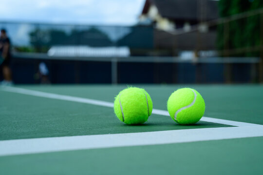 Tennis Balls Resting on Green Hard Court Surface with White Lines and Blurred Background