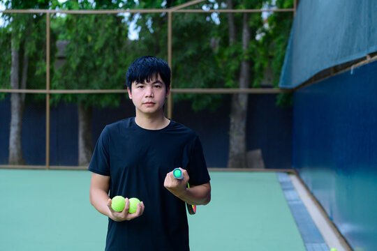 Young Asian Man Holding Tennis Balls and Racket on Outdoor Court Ready to Play