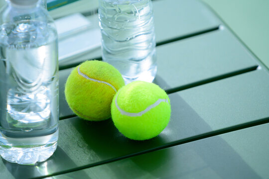 Two Tennis Balls and Water Bottles on Green Table