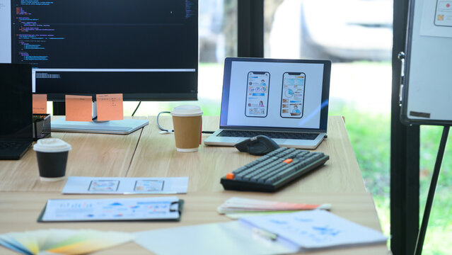 Developer Workspace Desk with Dual Monitor Code Editor and Laptop Showing Mobile App UI Design Wireframes