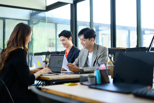 Young Asian Business Team Collaborating with Laptop and Documents in Modern Office