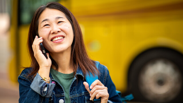 Smiling Asian woman talking on smart phone near bus