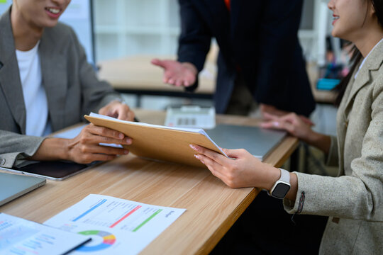 Business team exchanging documents during office meeting with charts and laptop on wooden desk