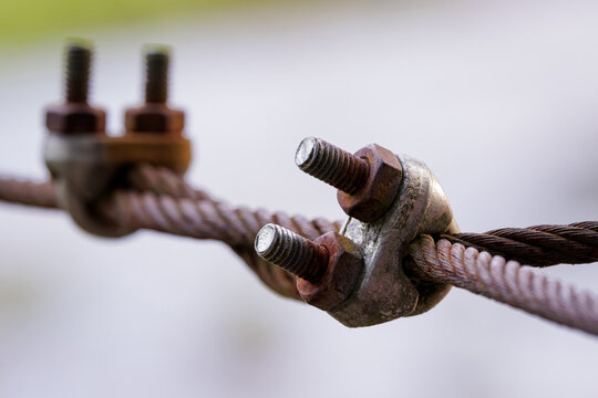 weathered steel wire rope secured with a rusted metal clamp and threaded bolts, highlighting industrial hardware, corrosion, texture, and mechanical detail against a soft blurred background