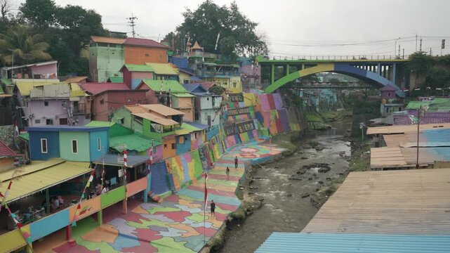 Wide view of vibrant painted houses and riverside walkway in Kampung Tridi, Malang