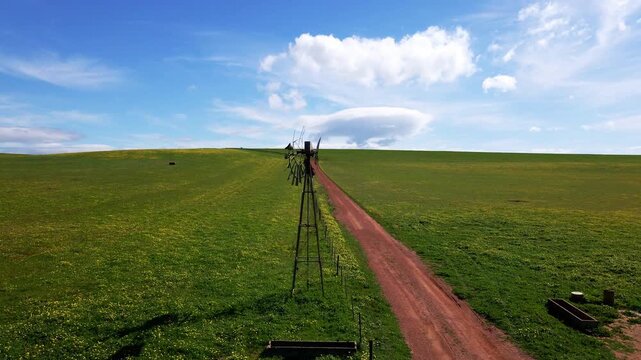 An old broken wind pump in the Overberg farming region of South Africa with a dirt road and anole fields and mountains in the distance