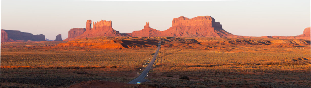 View of the iconic red sandstone buttes of Monument Valley at golden hour with a long road stretching through the desert landscape in Oljato-Monument Valley, Arizona, United States.