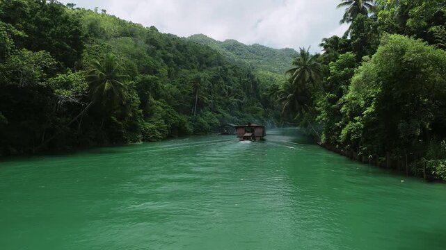 Aerial follow ascends behind a Loboc River cruise boat traveling through green water between forested hills in Bohol