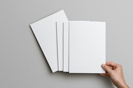 A hand holds a blank white brochure with a stack behind it