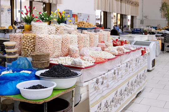Traditional dried cheese kurt displayed at an indoor bazaar stall in Bukhara, Uzbekistan. Colorful confections and raisins arranged on plates and in bags showcase local market abundance.