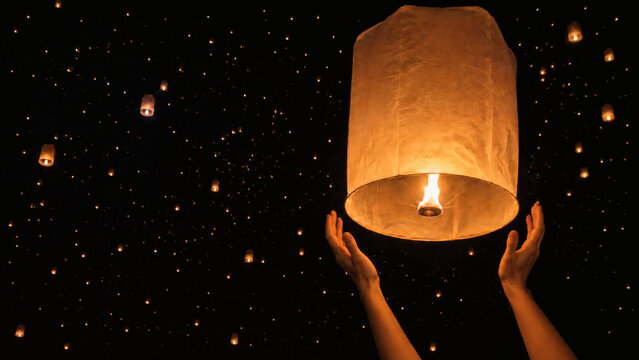 Hands Releasing Glowing Khom Loi Lantern During Yi Peng Festival at Night