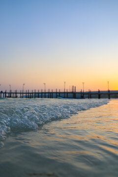 View of Koh Rong Sanloem pier at sunset with gentle waves breaking on the sandy shore in Preah Sihanouk, Sihanoukville, Cambodia.