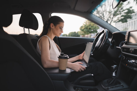 Woman using laptop while sitting in parked vehicle
