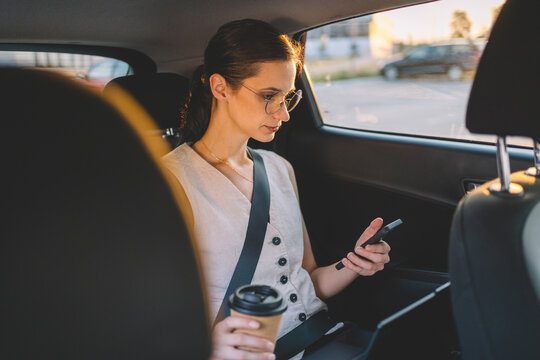 Businesswoman using smartphone and drinking coffee in car