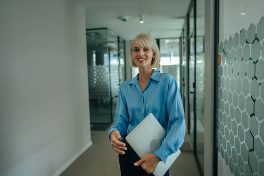 Businesswoman walking in modern office holding laptop