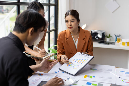 Business colleagues analyzing financial report data during meeting. Three businesspeople collaborating in an office, discussing company growth strategies and reviewing charts on a clipboard.