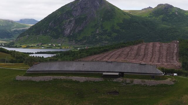 An aerial view shows the reconstructed chieftain longhouse at Lofotr Viking Museum surrounded by mountains and a lake in Borg, Lofoten, Norway.