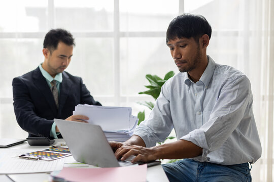 Businessmen collaborating on paperwork and laptop in office. Two Asian businessman diligently working in an office.