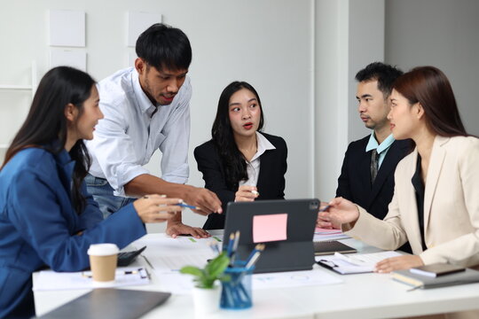 Asian business professionals discussing strategy and analyzing data on a tablet during a corporate meeting in office.