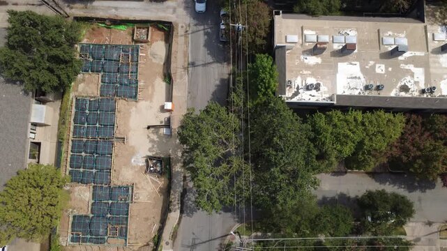 Subterranean concrete footings border lush tree canopies along Rawlins Street in Dallas. Cleared development parcels demonstrate rapid housing expansion across DFW Metroplex, Texas