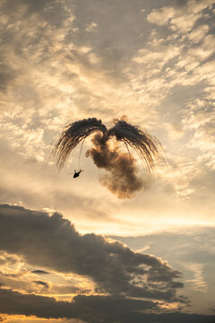 View of an NH-90 helicopter performing at the Antidotum Airshow, releasing flares in a dramatic wing-like pattern against a golden sunset sky in Leszno, Greater Poland Voivod, Poland.