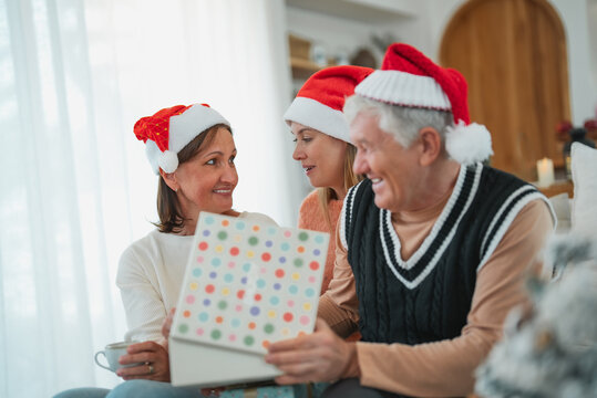 Senior parents and adult daughter looking at Christmas present together, sharing smiles and excitement during holiday celebration at home.