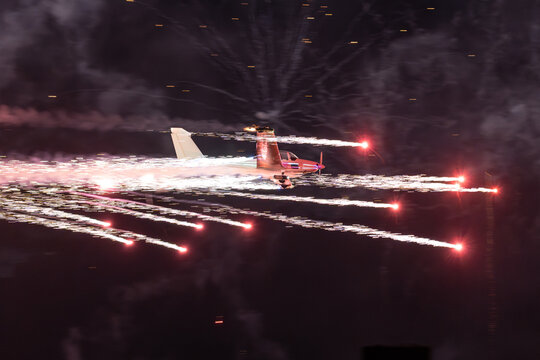 View of an aerobatic airplane performing at the Antidotum Airshow at Leszno Airport, trailing bright pyrotechnic sparks against the night sky in Leszno, Wielkopolskie, Poland.